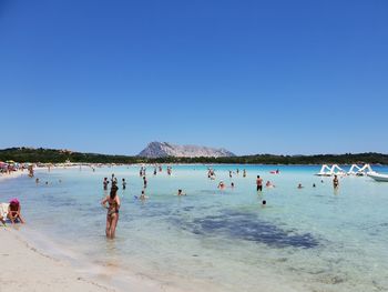 People on beach against clear blue sky