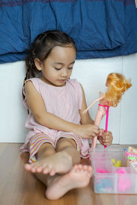 Cute girl playing with doll while sitting on floor at home