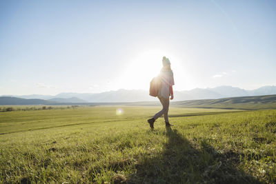 Full length of female hiker walking on grassy field against sky