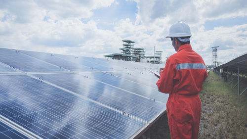 Engineer standing amidst solar panel against cloudy sky