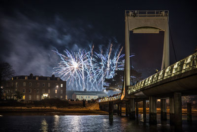 Firework display over river against sky in city at night