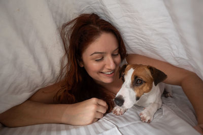 Caucasian red-haired woman sleeps in an embrace with a jack russell terrier dog on a white sheet