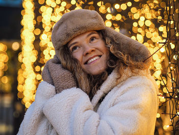 Portrait of young woman standing against illuminated christmas tree