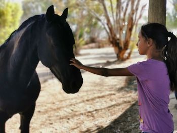 Girl stroking horse while standing on field