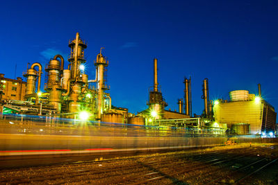 Illuminated factory against clear blue sky at night