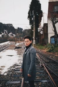 Portrait of young man standing on railroad track during winter