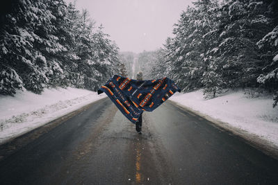 Rear view of woman with blanket walking on road amidst snow covered trees in forest