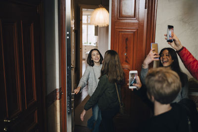 Happy friends photographing girls while standing at doorway