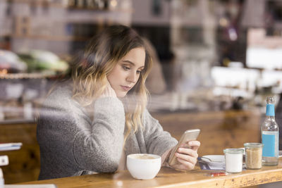 Portrait of sad young woman in a coffee shop looking at cell phone