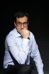 Portrait of young man sitting against black background