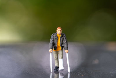 Miniature people , full length view of a man with broken leg is using crutch for walking