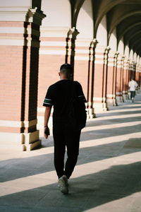 Rear view full length of teenage boy walking in corridor of building