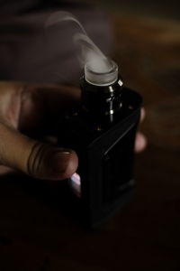 Cropped hand holding electronic cigarette with smoke at table