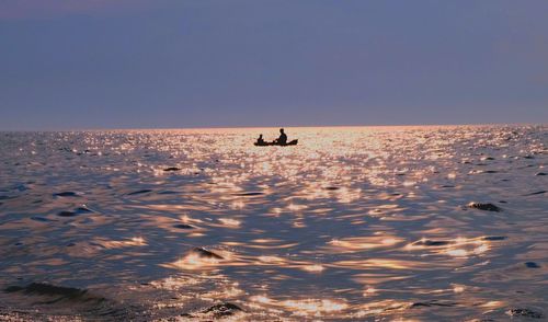 Silhouette person in a boat in sea against sky during sunset