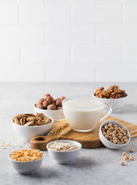 Vegetable milk in a mug on the background of bowls with nuts, oatmeal and legumes. 