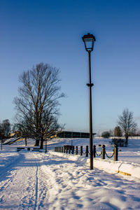 Street light on snow covered field against clear blue sky