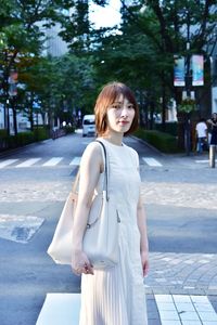 Portrait of young woman standing on road in city