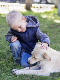 Cute boy playing with dog while kneeling on grassy field