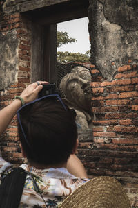 Rear view of woman photographing against wall