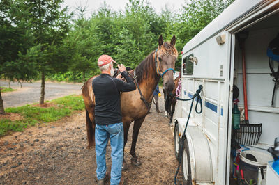 Rear view full length of man tying saddle on horse by van