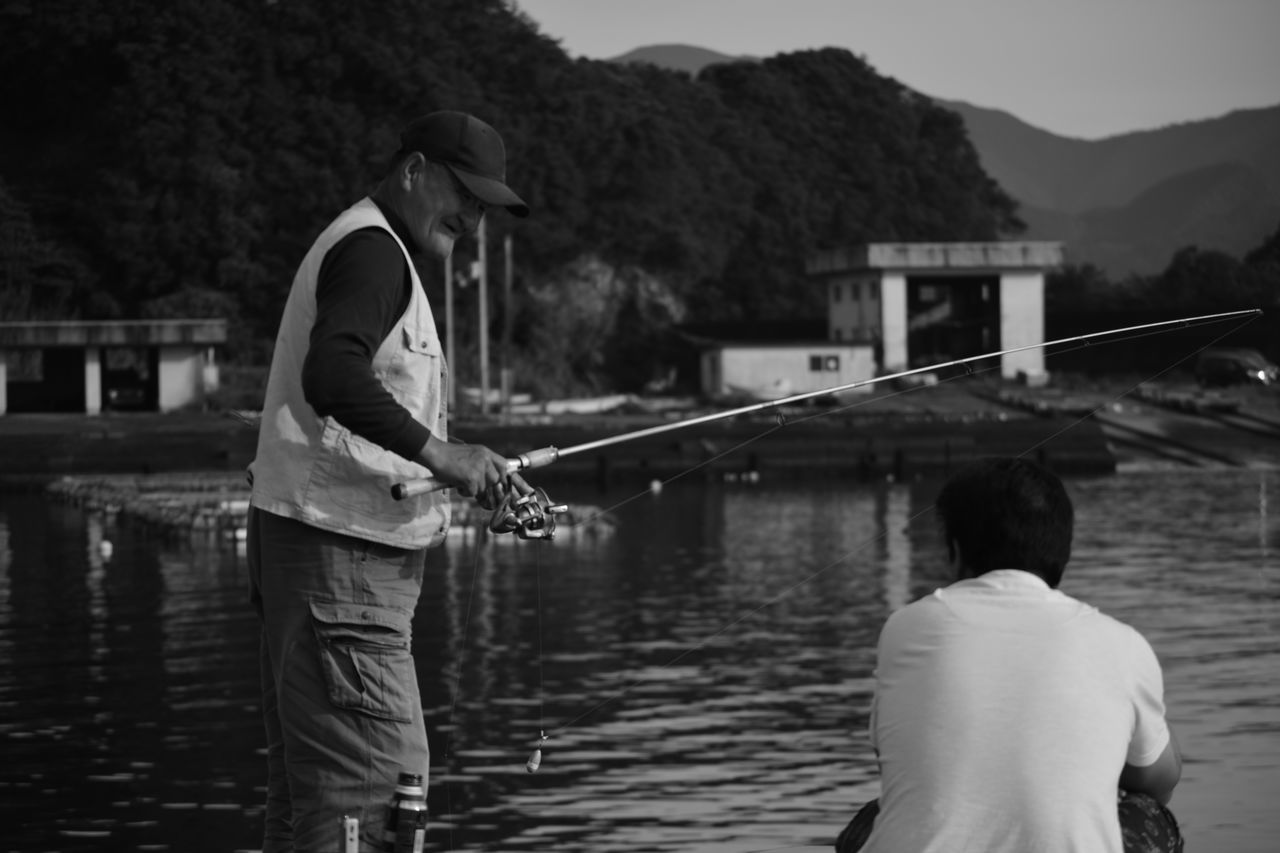 water, lifestyles, rear view, men, leisure activity, lake, casual clothing, mountain, river, standing, full length, three quarter length, person, nautical vessel, outdoors, built structure, fishing, holding