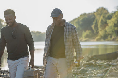 Male friends talking while walking on rocks by lake against sky