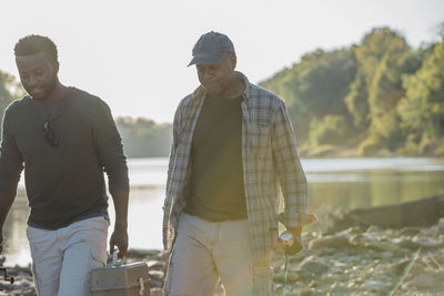 Male friends talking while walking on rocks by lake against sky