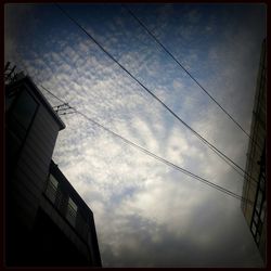 Low angle view of power lines against cloudy sky