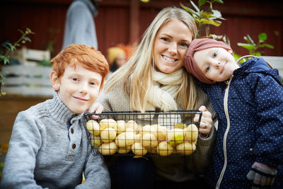 Portrait of mother with potato basket sitting by children at yard