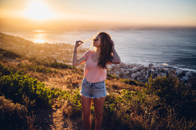 Woman standing by sea against sky during sunset