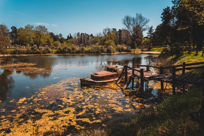 Old rusty abandoned wrecked ship tied up to a broken wooden dock in a small lake