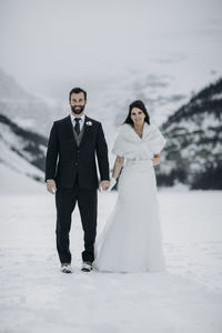 Newlywed bride and groom stand on frozen lake louise, canada in winter