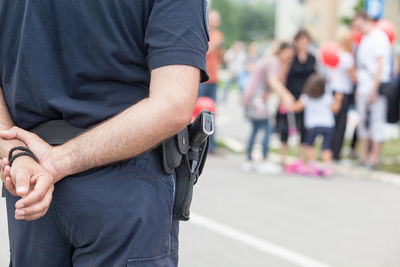 Midsection of police officer standing with hands behind back on street