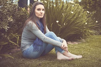 Side view portrait of young woman sitting by plants at park