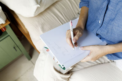 Woman writing in book sitting on bed at home