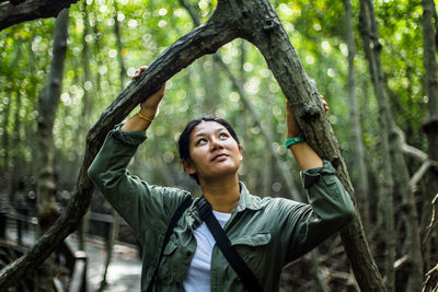 Smiling woman looking up while standing amidst trees in forest