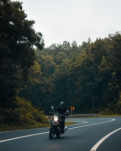 Man riding motorcycle on road against trees