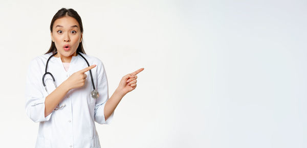 Portrait of female doctor standing against white background