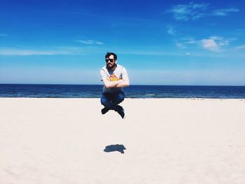 Full length of man sitting in mid-air over beach against sky