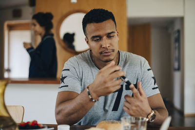 Man checking blood sugar level while having breakfast at home