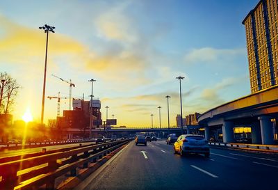 Cars on street against sky at sunset