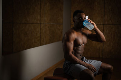 Shirtless african american man drinking from a shaker in the gym.