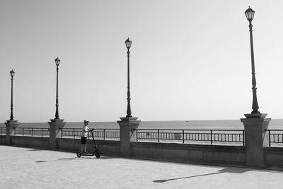 Street lights on footpath by sea against clear sky