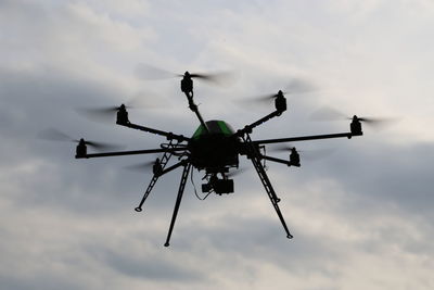 Low angle view of silhouette drone flying against cloudy sky during sunset