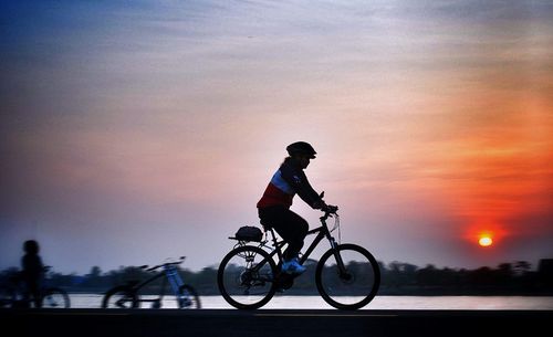 Side view of silhouette woman riding bicycle against sky during sunset