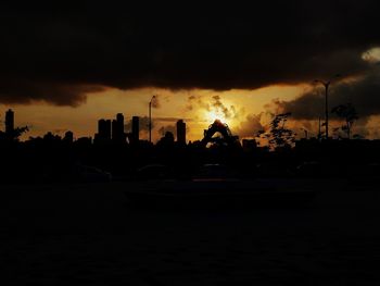 Silhouette city buildings against dramatic sky during sunset