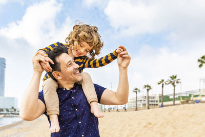 Spain, barcelona, father with son on the beach giving a piggyback ride