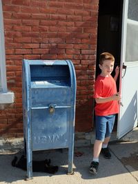 Boy exiting building by public mailbox on footpath