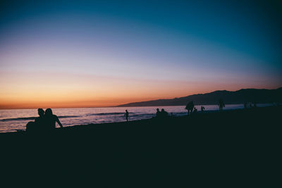 Silhouette people on beach against sky during sunset