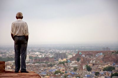 Rear view of man with hands in pockets standing on cliff